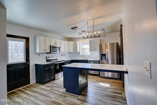 kitchen featuring stainless steel appliances, a barn door, light wood-style floors, white cabinetry, and a sink