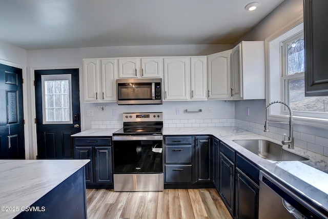 kitchen with appliances with stainless steel finishes, a healthy amount of sunlight, white cabinets, a sink, and light stone countertops