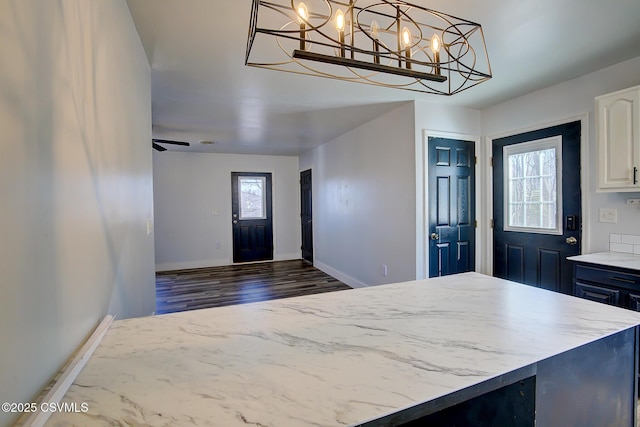 kitchen with decorative light fixtures, wood finished floors, white cabinets, light stone countertops, and baseboards