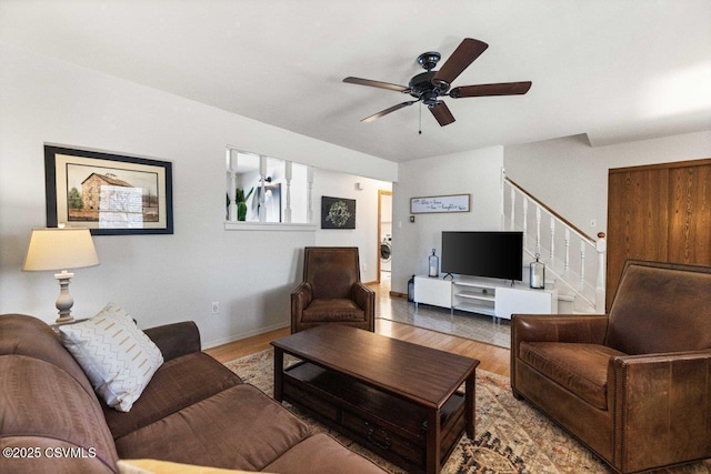 living room featuring baseboards, a ceiling fan, stairway, washer / clothes dryer, and light wood-style floors