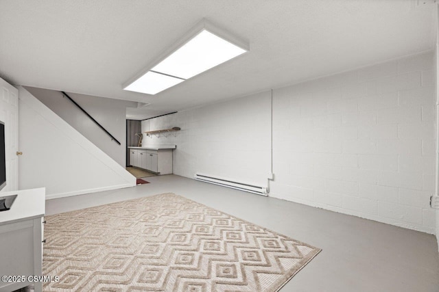 unfurnished living room featuring finished concrete flooring, stairway, baseboard heating, and concrete block wall