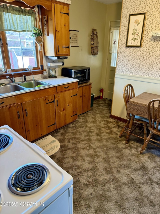 kitchen with light countertops, brown cabinetry, a sink, and electric stove