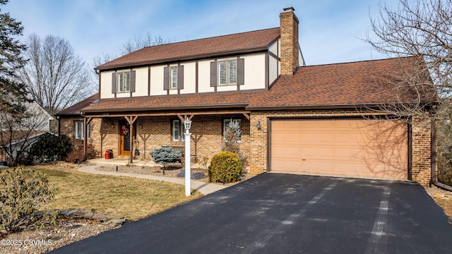 tudor home with a garage, driveway, stucco siding, a chimney, and brick siding