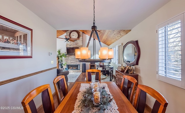 dining area featuring a healthy amount of sunlight, a chandelier, a stone fireplace, and lofted ceiling