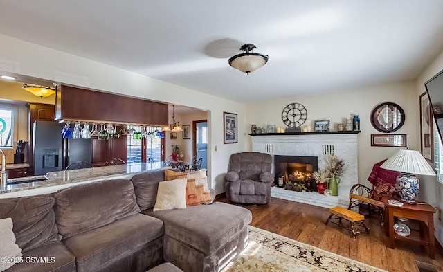 living room with a brick fireplace, a chandelier, and wood finished floors