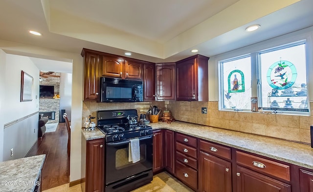 kitchen featuring black appliances, tasteful backsplash, a fireplace, and light stone countertops