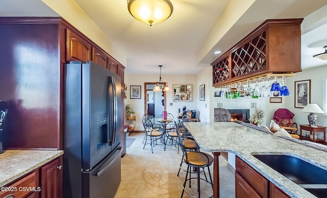 kitchen featuring a lit fireplace, light stone counters, pendant lighting, and black fridge with ice dispenser