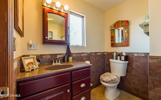 bathroom featuring toilet, a wainscoted wall, tile patterned flooring, vanity, and tile walls