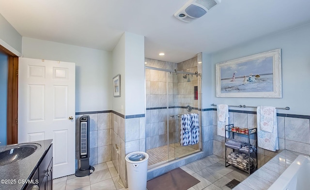 full bathroom with a wainscoted wall, a stall shower, tile patterned flooring, and tile walls