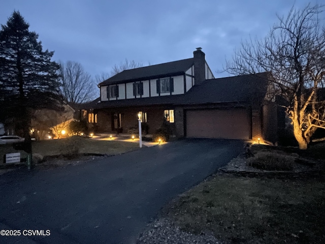 tudor house with driveway, a chimney, and an attached garage