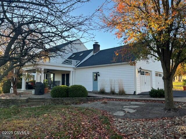 back of house with covered porch, a chimney, and an attached garage