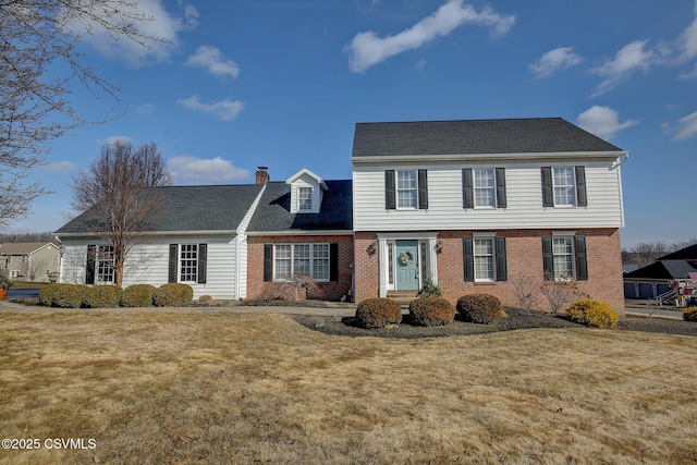 colonial house with a chimney, a front lawn, and brick siding