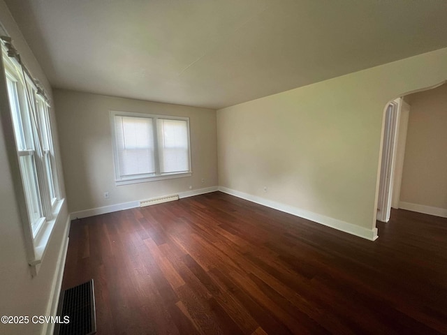 unfurnished room with dark wood-type flooring, arched walkways, visible vents, and baseboards