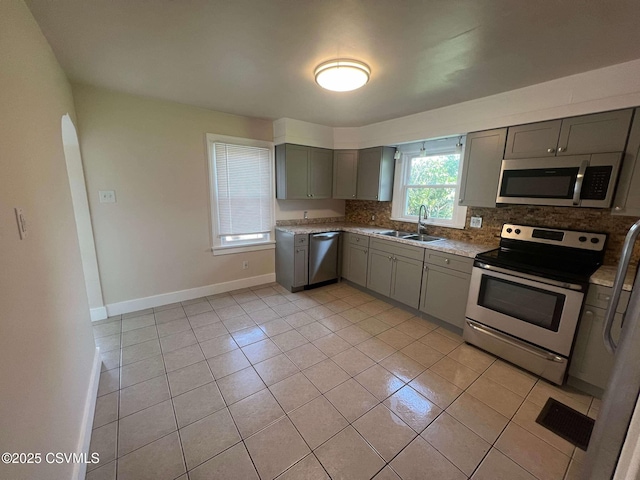 kitchen featuring light tile patterned floors, a sink, appliances with stainless steel finishes, gray cabinets, and decorative backsplash