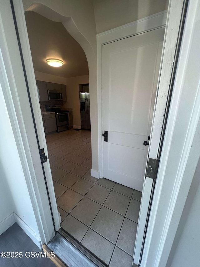 hall featuring arched walkways, tile patterned flooring, and baseboards