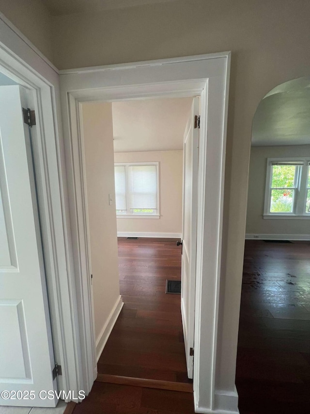 corridor with arched walkways, dark wood-type flooring, visible vents, and baseboards