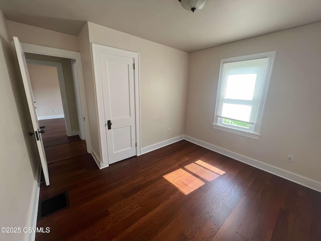 unfurnished bedroom featuring baseboards, a closet, visible vents, and dark wood-style flooring