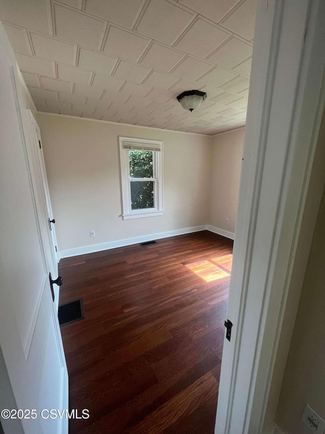 unfurnished room featuring dark wood-style flooring, visible vents, and baseboards