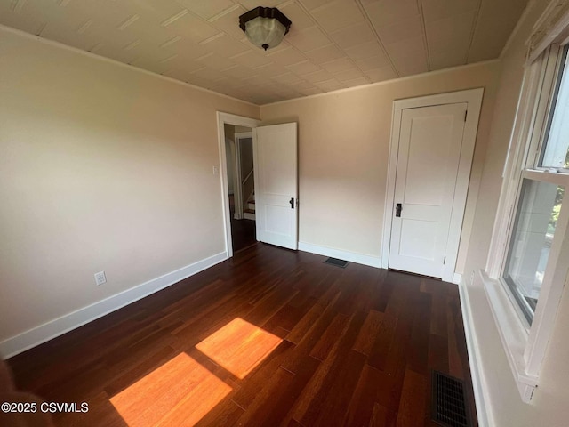 unfurnished bedroom with dark wood-type flooring, visible vents, and baseboards