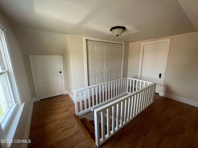 hall featuring dark wood-type flooring, an upstairs landing, and baseboards