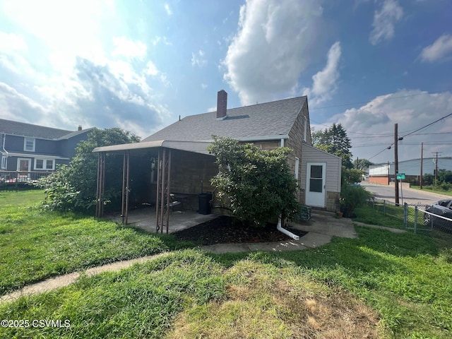 rear view of property featuring a shingled roof, a lawn, a chimney, and fence