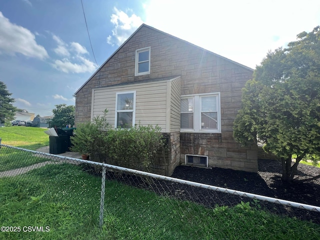 view of side of home with a yard, stone siding, and fence