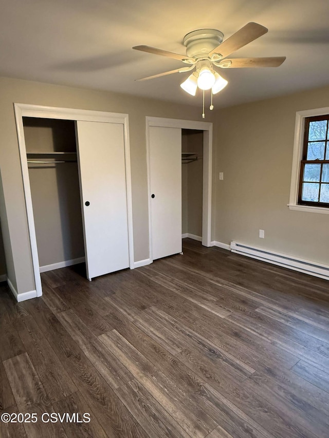 unfurnished bedroom with dark wood-style floors, a baseboard radiator, two closets, and baseboards