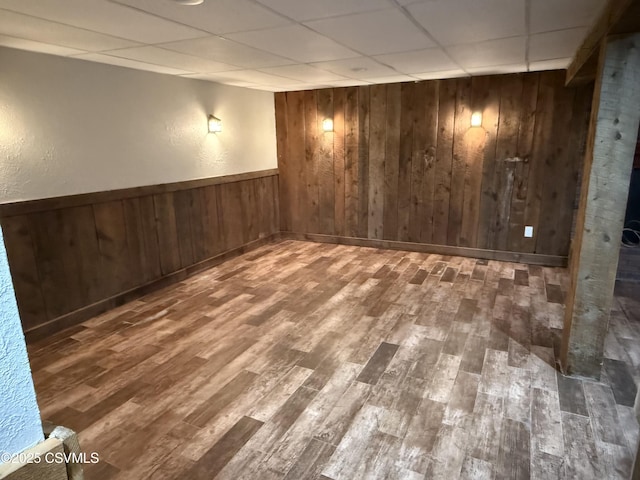 finished basement featuring a wainscoted wall, a drop ceiling, wood finished floors, and wooden walls