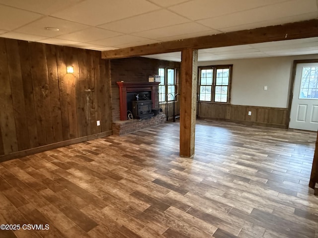 below grade area featuring a wood stove, a drop ceiling, wooden walls, and wood finished floors