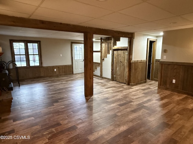 below grade area featuring stairs, dark wood-type flooring, a drop ceiling, and wainscoting