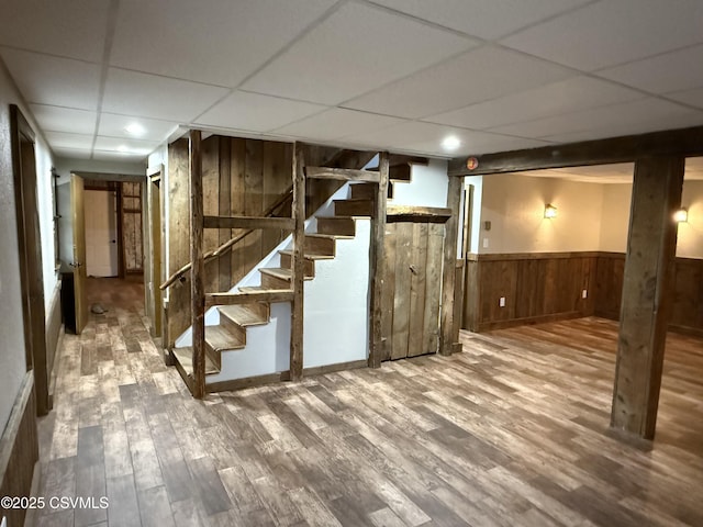 finished basement featuring a drop ceiling, wood walls, wood finished floors, stairway, and wainscoting