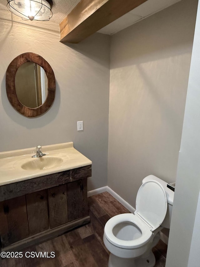 half bath with toilet, baseboards, wood finished floors, and vanity