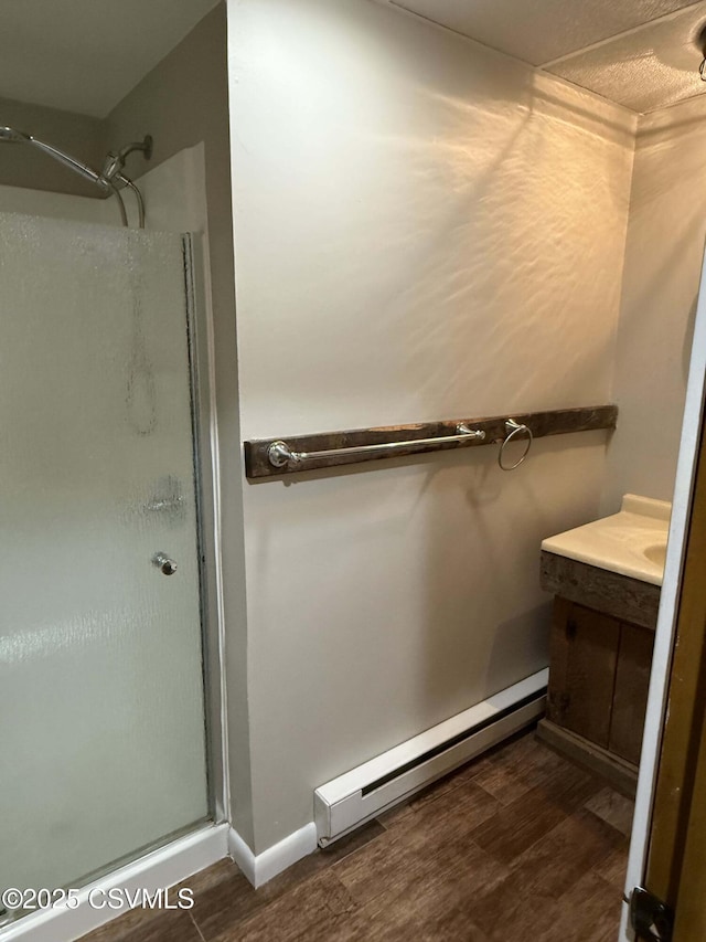 bathroom with a baseboard heating unit, a shower stall, vanity, and wood finished floors