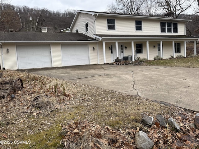 view of front of property featuring driveway, a chimney, an attached garage, covered porch, and cooling unit