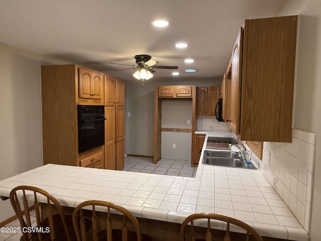 kitchen with tile counters, tasteful backsplash, a sink, a peninsula, and black appliances