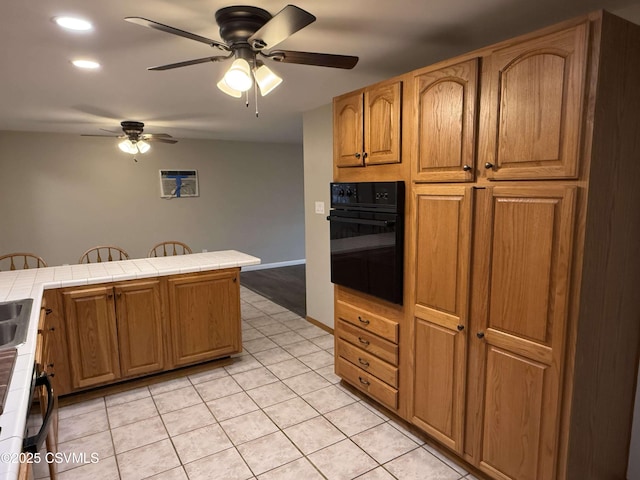 kitchen featuring tile countertops, light tile patterned floors, brown cabinetry, and oven