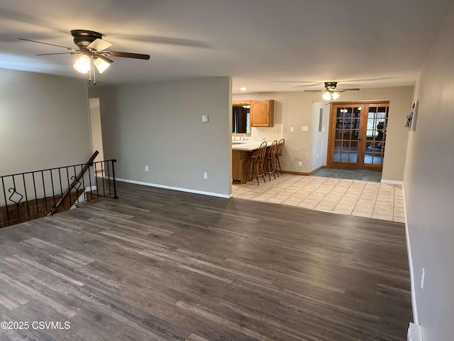 unfurnished living room featuring french doors, ceiling fan, baseboards, and wood finished floors