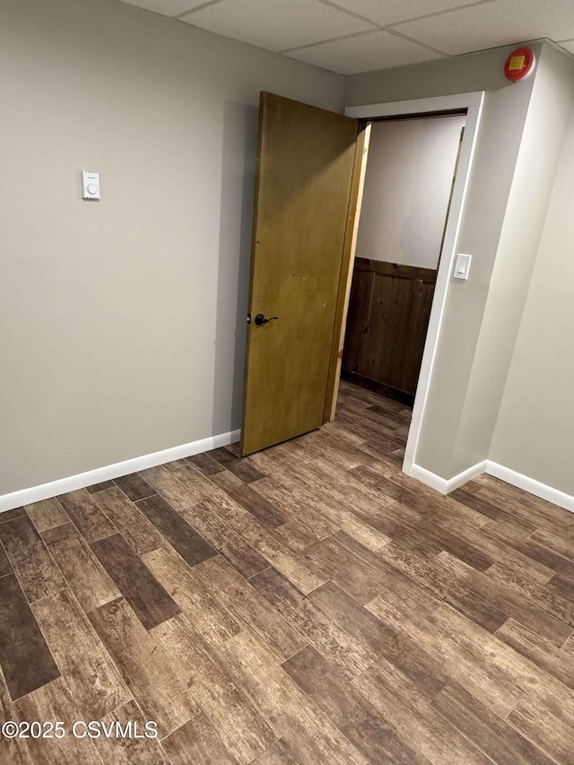 empty room featuring a paneled ceiling, baseboards, and wood finished floors