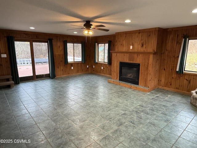 unfurnished living room featuring wood walls, recessed lighting, a glass covered fireplace, and baseboards