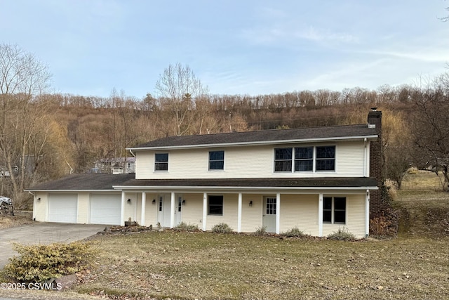 view of front facade featuring driveway, a chimney, a porch, an attached garage, and a front lawn