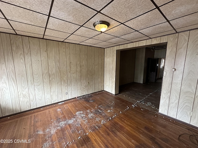 unfurnished room featuring a paneled ceiling, dark wood-style flooring, wood walls, and baseboards