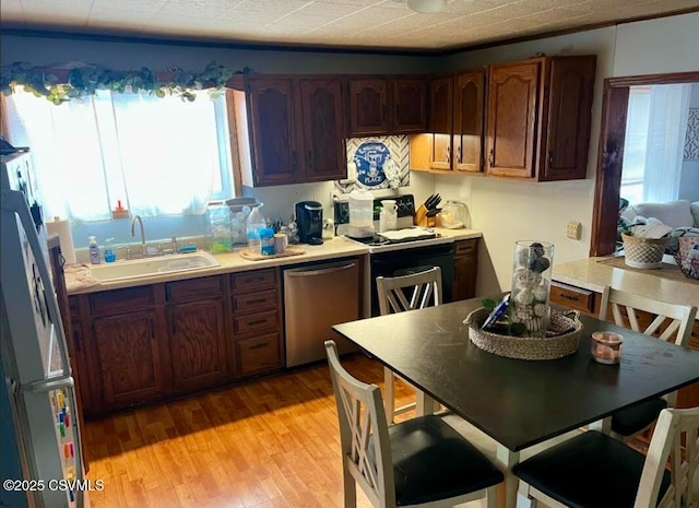 kitchen featuring light wood finished floors, dishwasher, freestanding refrigerator, light countertops, and a sink