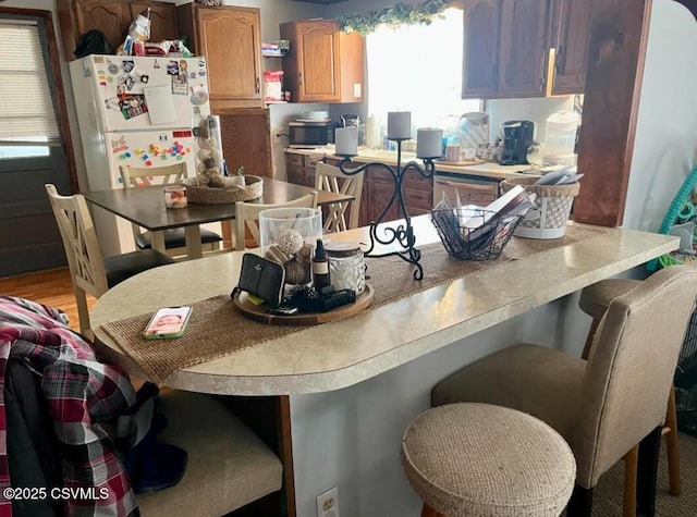 kitchen with a breakfast bar area, light countertops, stainless steel microwave, light wood-style floors, and freestanding refrigerator