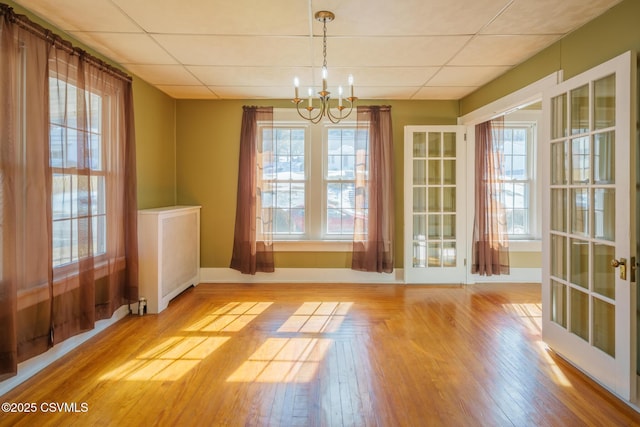 unfurnished dining area with a paneled ceiling, french doors, a notable chandelier, and light wood-style flooring