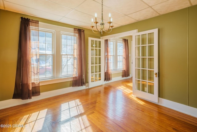 unfurnished dining area with baseboards, parquet flooring, a paneled ceiling, and a notable chandelier