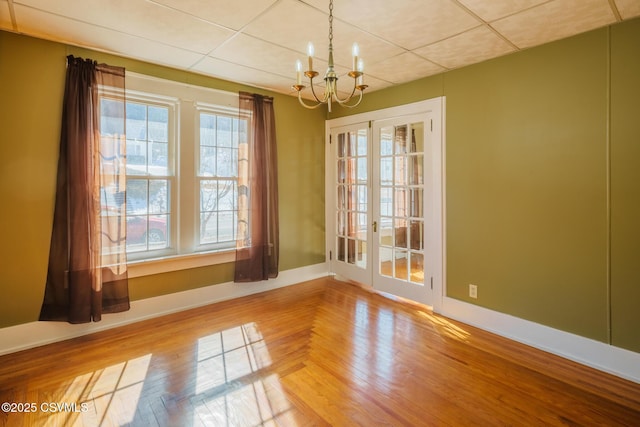 unfurnished room featuring baseboards, a chandelier, wood finished floors, and french doors