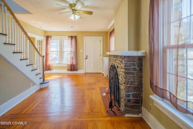 living room with stairway, ceiling fan, a stone fireplace, and baseboards