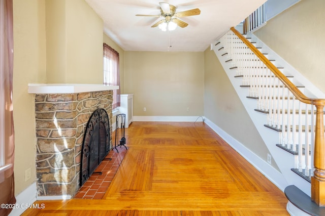 unfurnished living room with stairs, a fireplace, baseboards, and a ceiling fan