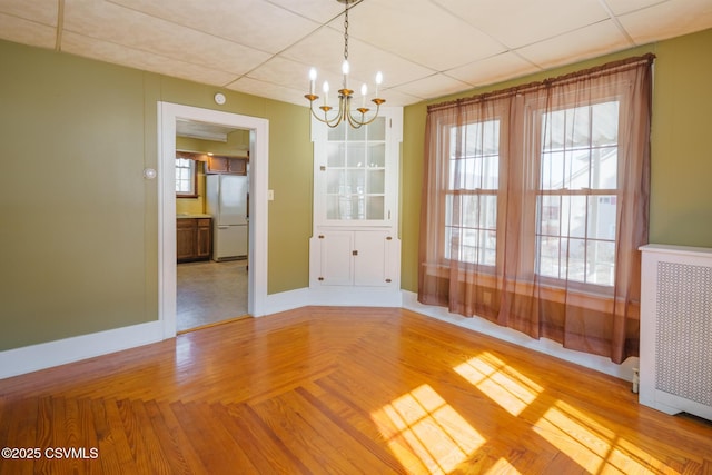 unfurnished dining area with a notable chandelier, a paneled ceiling, radiator heating unit, baseboards, and parquet flooring