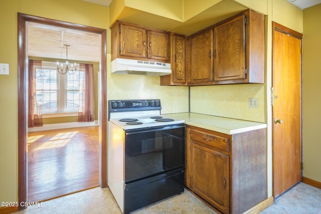 kitchen with pendant lighting, brown cabinets, light countertops, black electric range oven, and under cabinet range hood